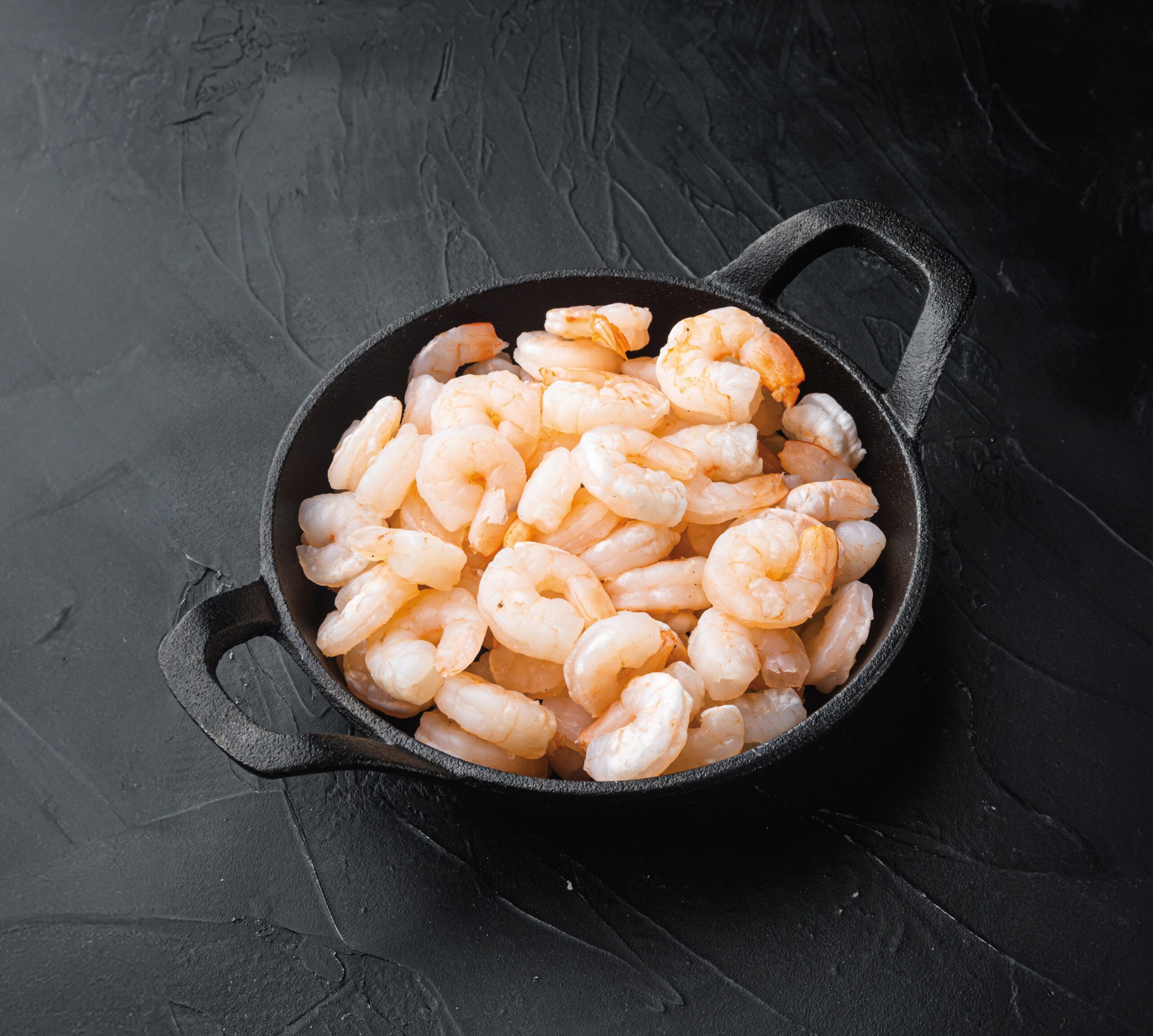 Boiled peeled shrimp prawns cooked, in frying cast iron pan or pot, on black stone background, with copy space for text